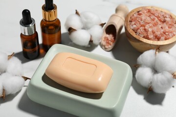 Soap bar, cosmetic products and cotton flowers on white table, above view