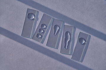 Samples of serum or micellar water on slides on a blue background with streaks of shadows.