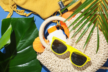 Beach accessories and palm leaves on blue background, flat lay