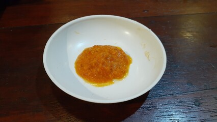 A plate of chili sauce on a wooden table.