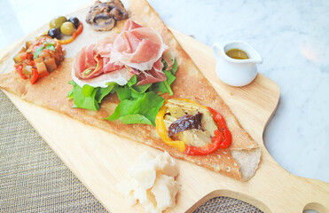 Appetizer Crepe or Crepe Antipasto with cold cuts and variety of saute vegetables served on wooden breadboard