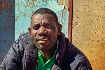 africa village, african man smiling , in front of the house in the yard, blue door,