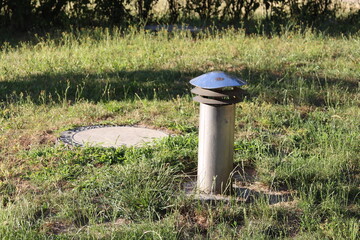 Modern street lamp with cylindrical design standing in grassy area beside paved pathway in urban...