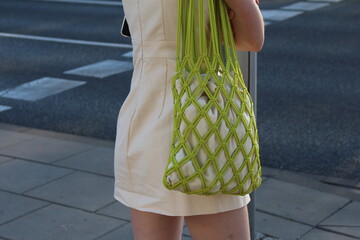 Green diamond-patterned textile bag held by person in light clothing displaying fashionable...