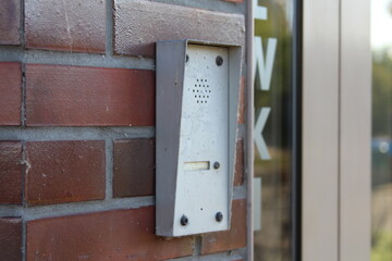 White electronic device or intercom system mounted on red brick wall beside glass door entrance