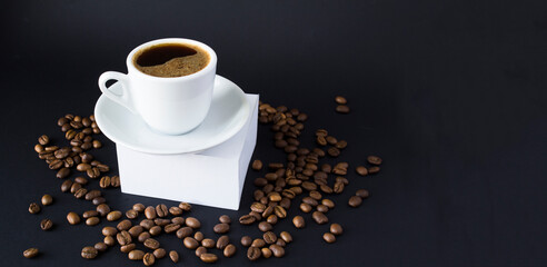 Black coffee in the white cup that stands on a white podium on a black background. Copy space.