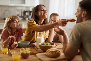 Happy family having a meal at dining table while woman is feeding her husband.