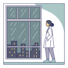 A thoughtful female doctor in a white lab coat stands by a large window looking out at a rainy city skyline at night