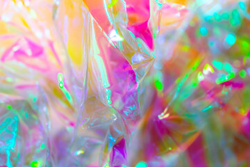 Close-up of iridescent crinkled cellophane foil with vibrant reflections in pink, yellow, green,...