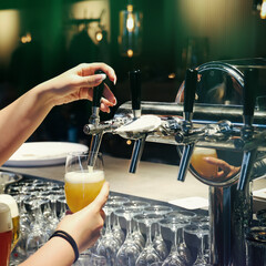 Beer being poured from a tap into a glass in a modern bar. Close-up of bartender’s hands and fresh draft beer. Elegant evening atmosphere.