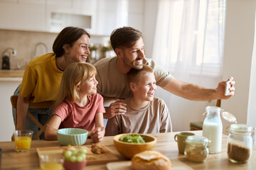 Happy family having fun while taking a selfie during breakfast in dining room