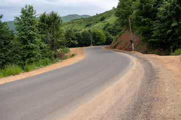 Winding mountain road surrounded by dense green forest and rolling hills