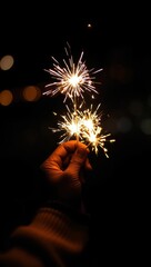 Hand holding sparklers glowing brightly against a dark night sky, creating a festive and magical...