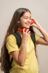 A happy young student laughs while putting on red headphones to listen to music.