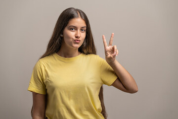 Playful young woman making a peace sign gesture with a fun expression in a studio.
