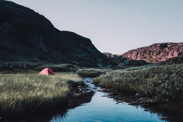 Remote red tent pitched beside a mountain stream in lush green grass
