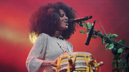 Talented artist with a natural hairstyle playing traditional percussion during a live concert dancing on stage in slow motion