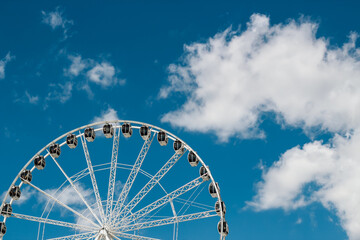 Ferris wheel against a clear blue sky with fluffy white clouds in the afternoon