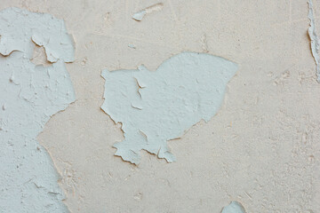 Cracked and peeling paint on a textured wall in a sunlit room revealing layers beneath