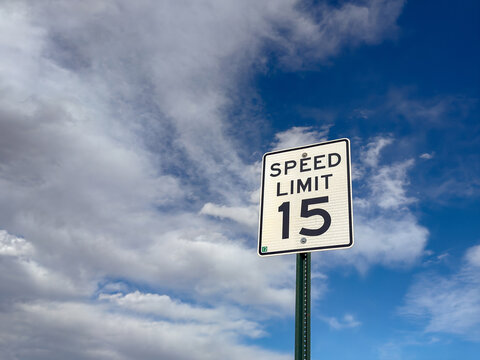 Speed limit sign for 15mph isolated against a blue sky with white clouds. No people. Copy space.