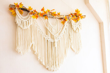 Macrame wall hanging decorated with autumn leaves in a cozy indoor setting
