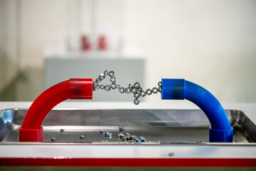 Red and blue magnetic pipes attract metal nuts and chains, illustrating fundamental physics...