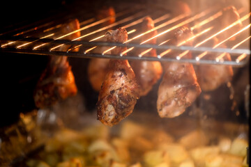 Chicken drumsticks roasting in an oven, dripping juices onto a tray below. The warm glow highlights the crispy texture, creating an appetizing and savory scene