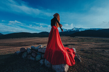 Young beautiful woman in red dress posing in high mountains