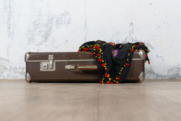 Vintage old classic travel leather suitcase circa 1940-60s with a vintage scarf. Travel luggage concept. Retro brown suitcase on a white wall background.