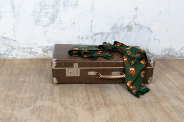 Vintage old classic travel leather suitcase circa 1940-60s with a vintage scarf. Travel luggage concept. Retro brown suitcase on a white wall background.