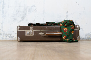 Vintage old classic travel leather suitcase circa 1940-60s with a vintage scarf. Travel luggage concept. Retro brown suitcase on a white wall background.