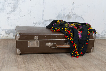 Vintage old classic travel leather suitcase circa 1940-60s with a vintage scarf. Travel luggage concept. Retro brown suitcase on a white wall background.