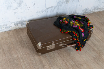 Vintage old classic travel leather suitcase circa 1940-60s with a vintage scarf. Travel luggage concept. Retro brown suitcase on a white wall background.