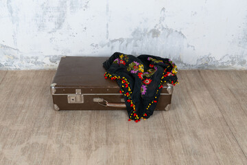 Vintage old classic travel leather suitcase circa 1940-60s with a vintage scarf. Travel luggage concept. Retro brown suitcase on a white wall background.