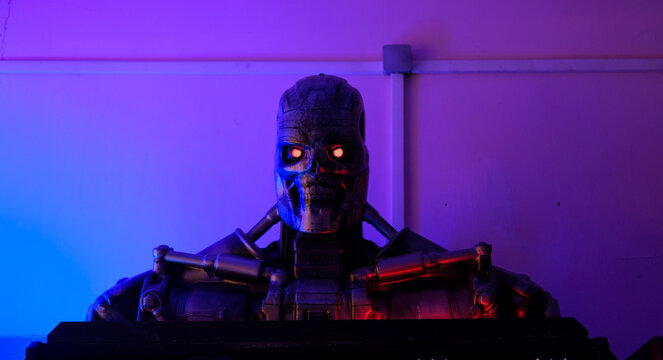 A Terminator-inspired robot figure with glowing red eyes, illuminated with purple and blue lighting in a dark setting.