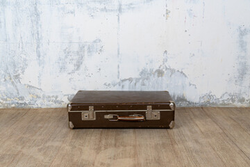 A vintage old brown travel leather suitcase lies on the wooden floor, Retro suitcase on a white wall background. Travel luggage concept.