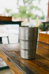 Cold Metal Drink Cup with Straw on Wooden Table in Outdoor Setting Surrounded by Nature