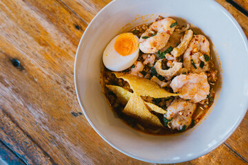 Delicious bowl of spicy shrimp soup with boiled egg, crispy toppings, and fresh herbs on a rustic wooden table