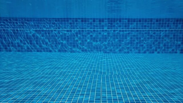 Tranquil underwater view of clear blue swimming pool with tile floor and water reflection.