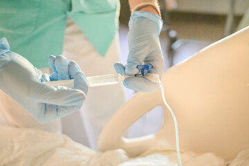 Unrecognizable nurse injects medication into the intravenous infusion device of a patient in the...
