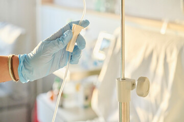 Nurse’s gloved hand adjusts the intravenous flow valve delivering medication through an infusion...