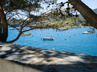 A peaceful harbor scene features a small boat floating on calm waters. Lush green trees frame the...
