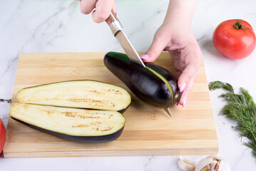 Cutting eggplant into two halves with a knife.