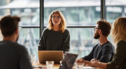 A woman leads a small group meeting around a table, presenting to attentive colleagues near a large window