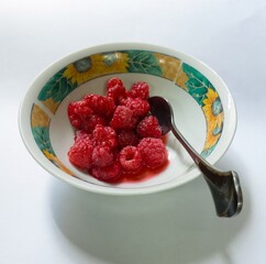 very ripe red raspberry with juice in a small saucer with a teaspoon