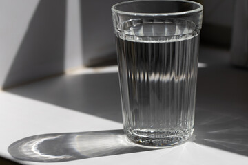 A cut glass of water standing on a white shelf