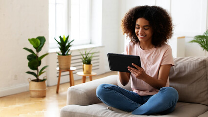Young woman with curly hair using tablet on couch living room plants