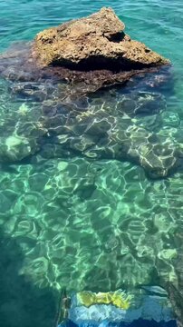 Crystal clear turquoise sea water with sun reflections shimmering over rocks and stones near the coast of Antalya, Turkey. Peaceful summer scene with underwater textures and natural sunlight patterns