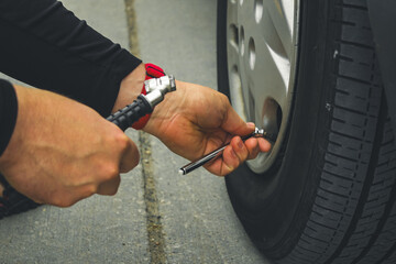 close-up of a person using a tire gauge to measure the air pressure inside a vehicle's tires while...