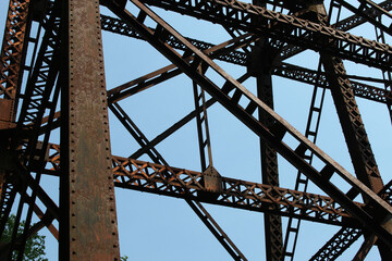 looking up at a weathered metal railroad bridge truss isolated against a blue sky